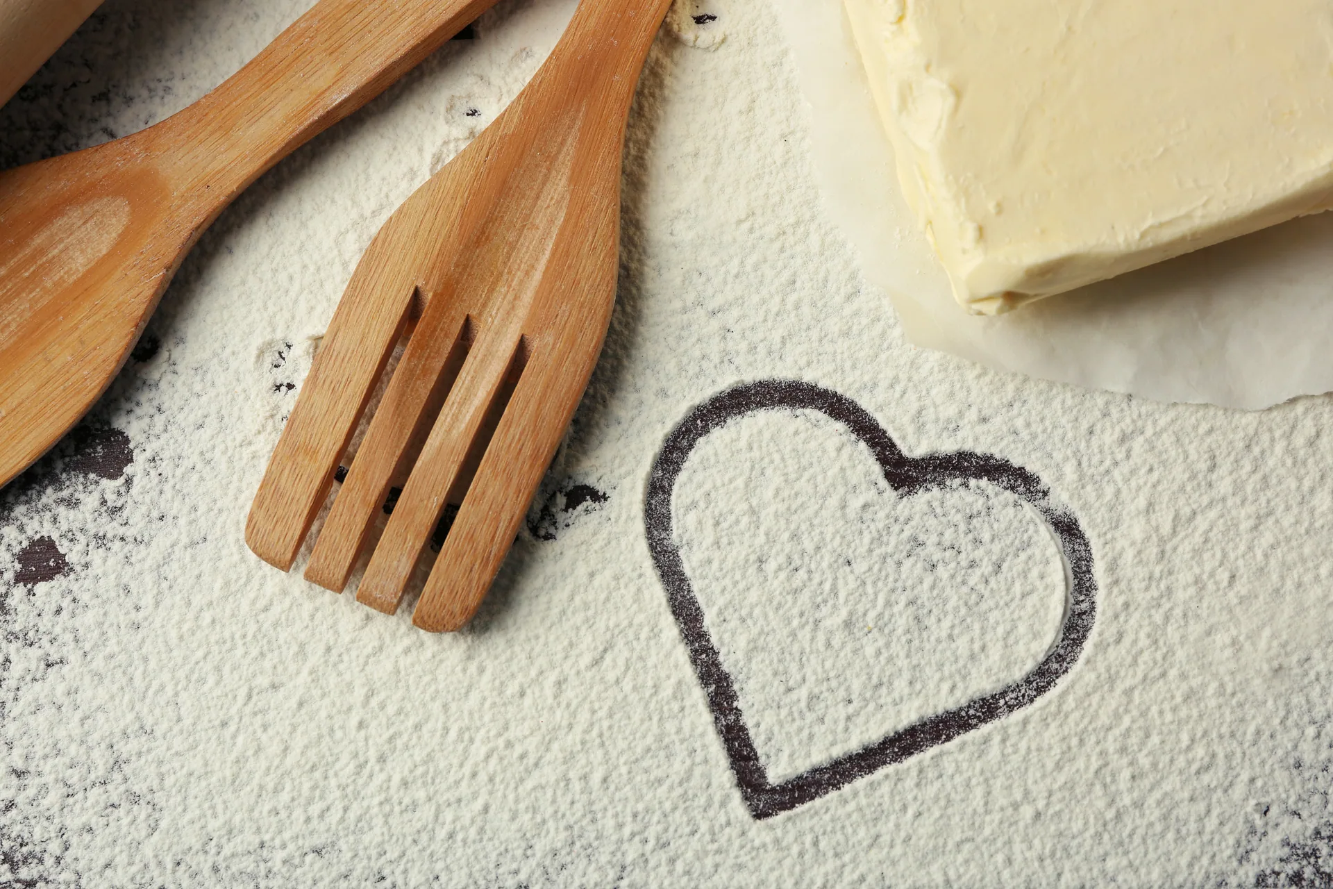 A heart drawn in flour next to wooden utensils and butter